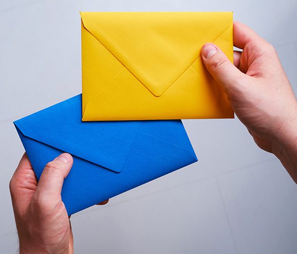 A man holds a yellow and blue paper envelope in his hand. New mail, message. Postal service. The person wants to send or receive a letter. Empty envelope, empty space. People communication concept